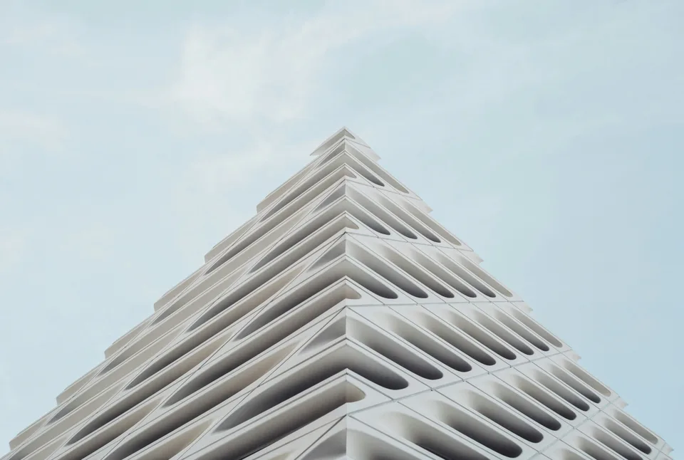 A white building facade of repeating curved panels, seen from below against a pale sky.